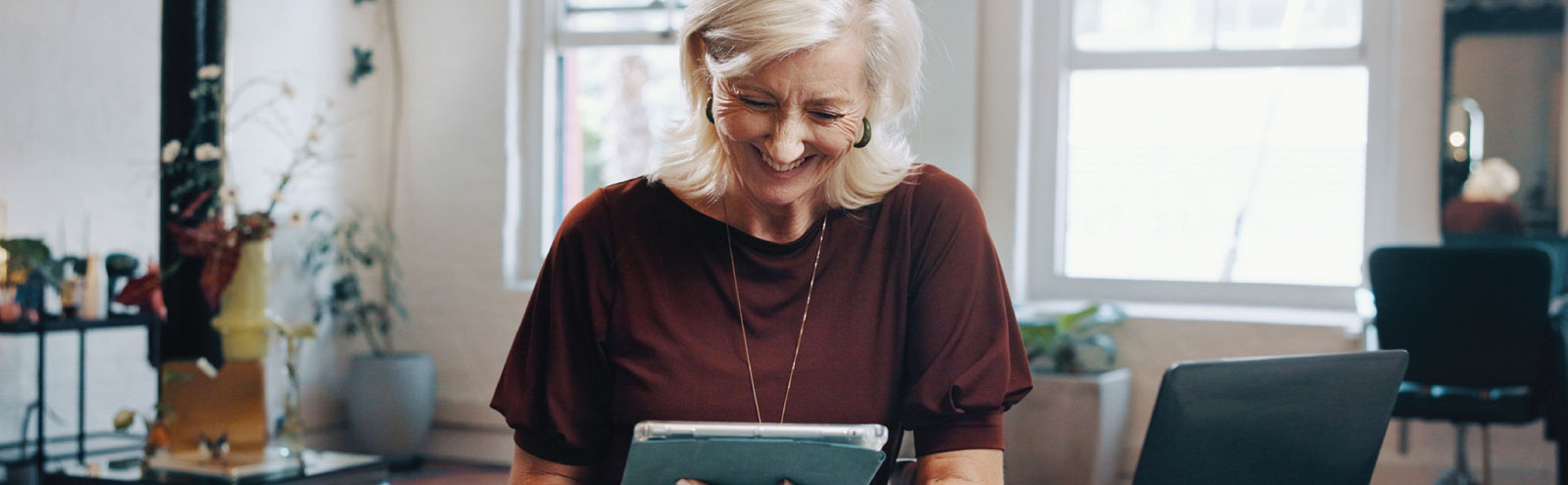 Mature woman in burgundy working on tablet.
