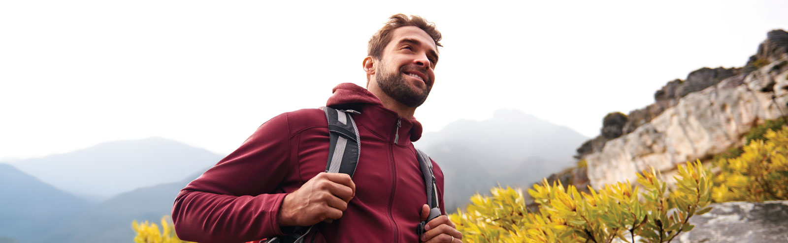Smiling man in burgundy hiking in the mountains.