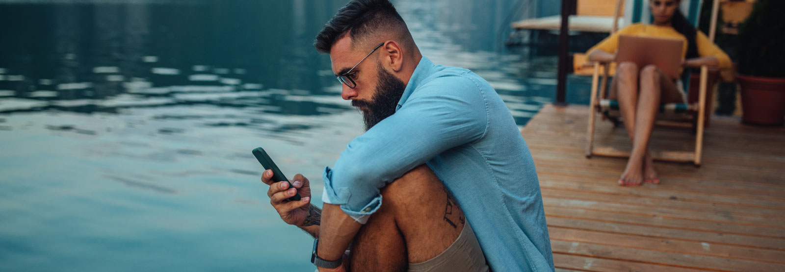 Man using his phone on a dock by the lake.