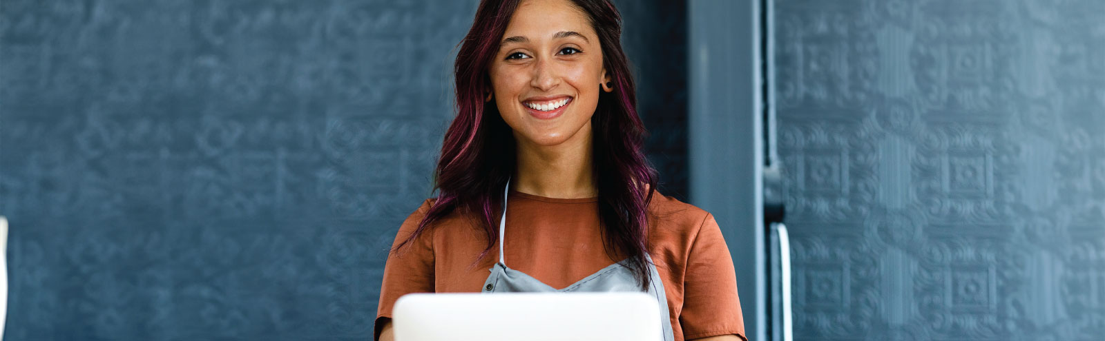 Female business owner smiling at register in front of a blue wall.