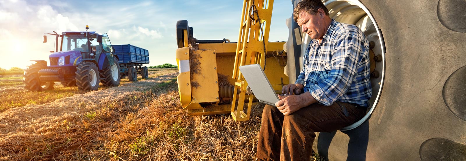 A farmer using laptop computer around agricultural equipment