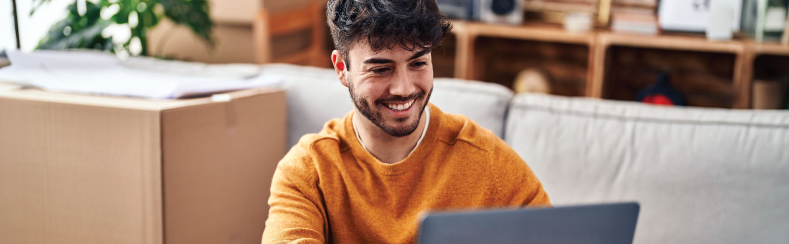 Man in gold working on a laptop next to a moving box.