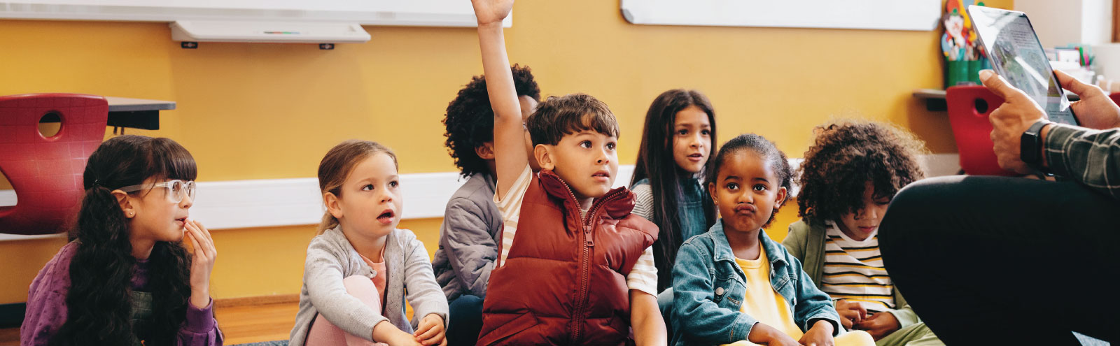 Elementary school child raising his hand in class among other students.