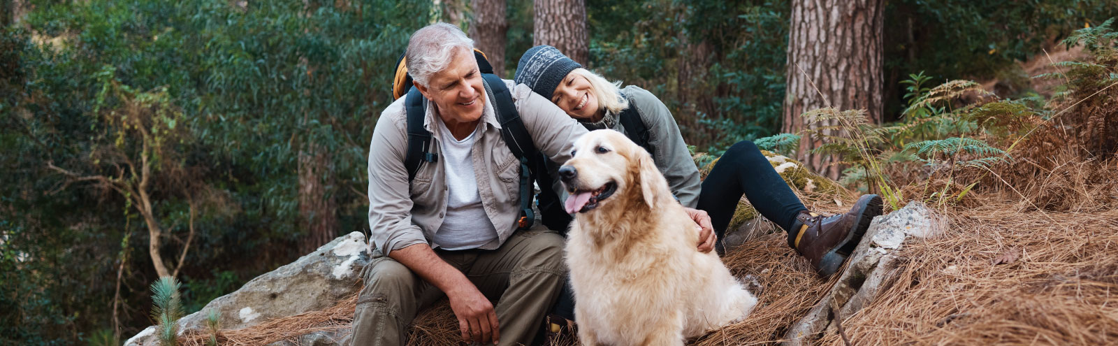Older man and woman in the mountains with their golden retriever.