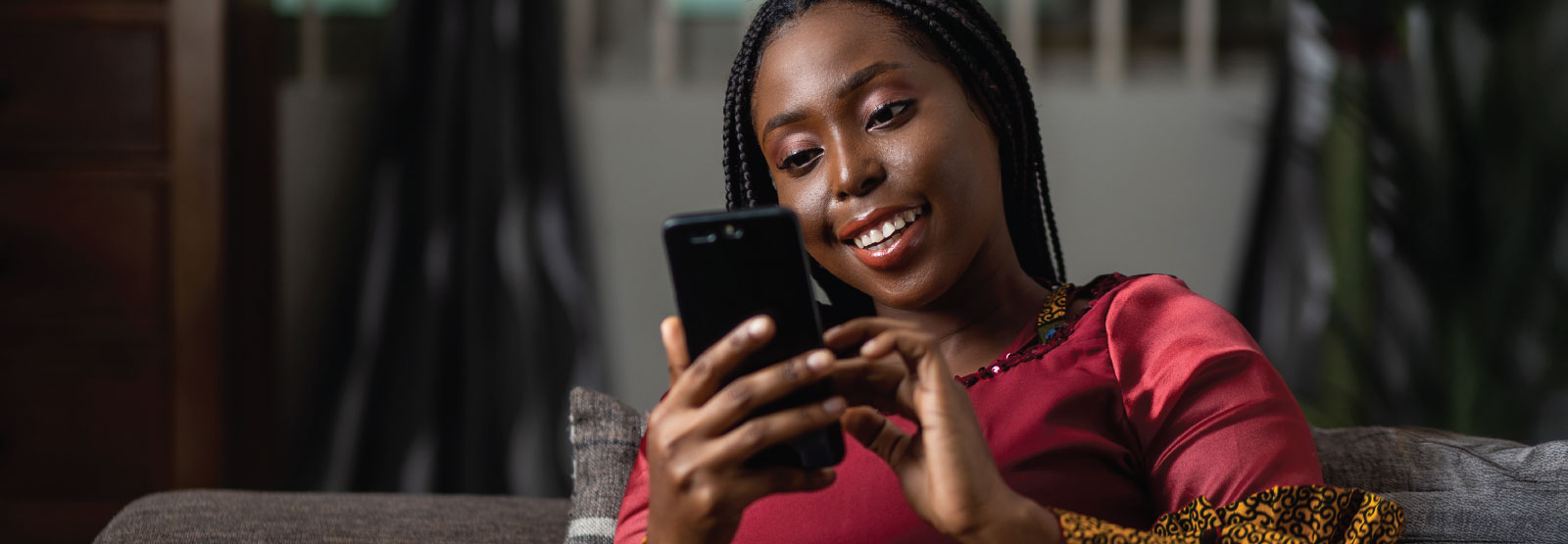 Woman in burgundy smiling while using her cell phone.