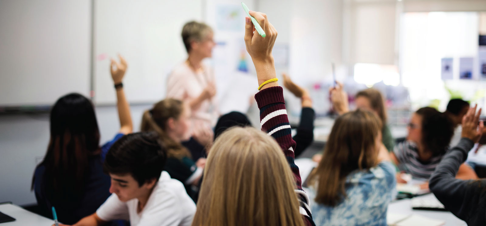 Back of student raising hand in a classroom.